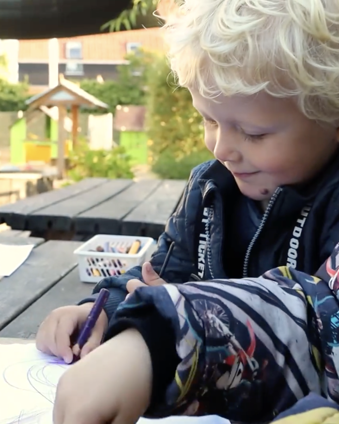 Tre børn tegner ved et bord udenfor